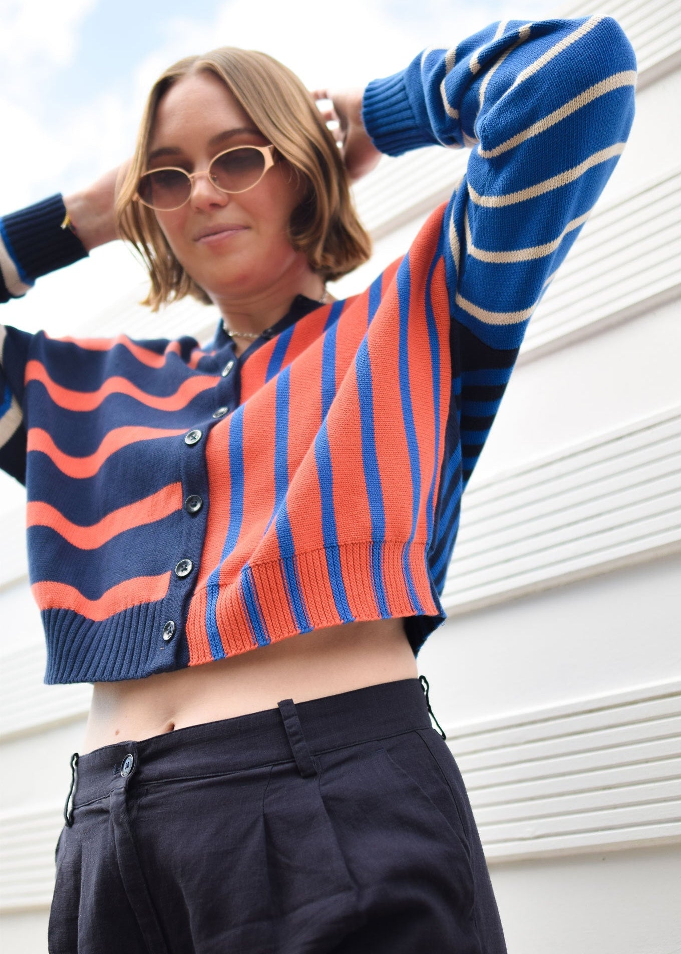 Person wearing a colorful striped sweater and sunglasses against a light-colored wall.