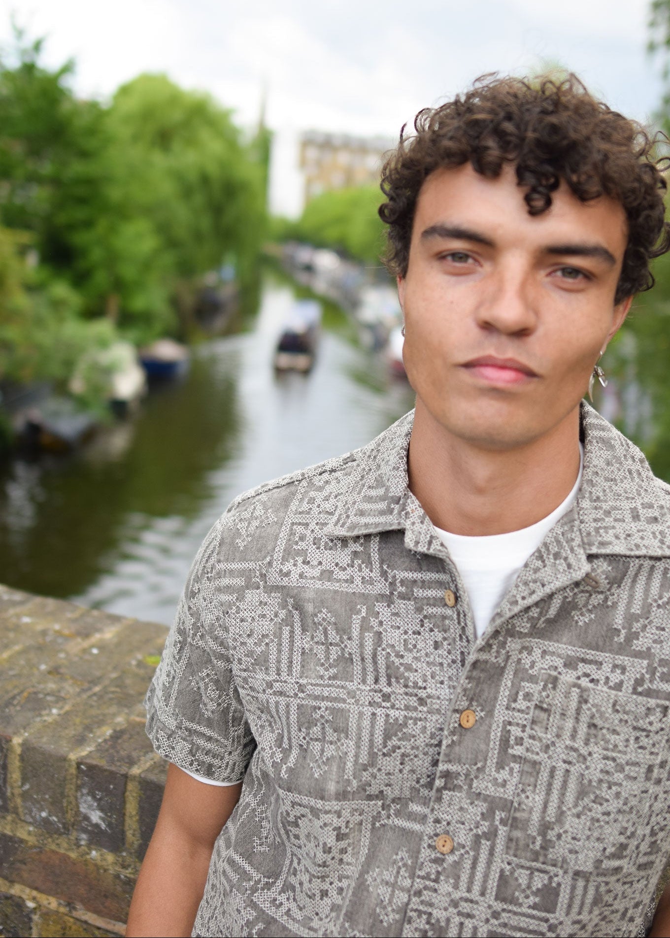 Person standing by a canal with boats and greenery in the background
