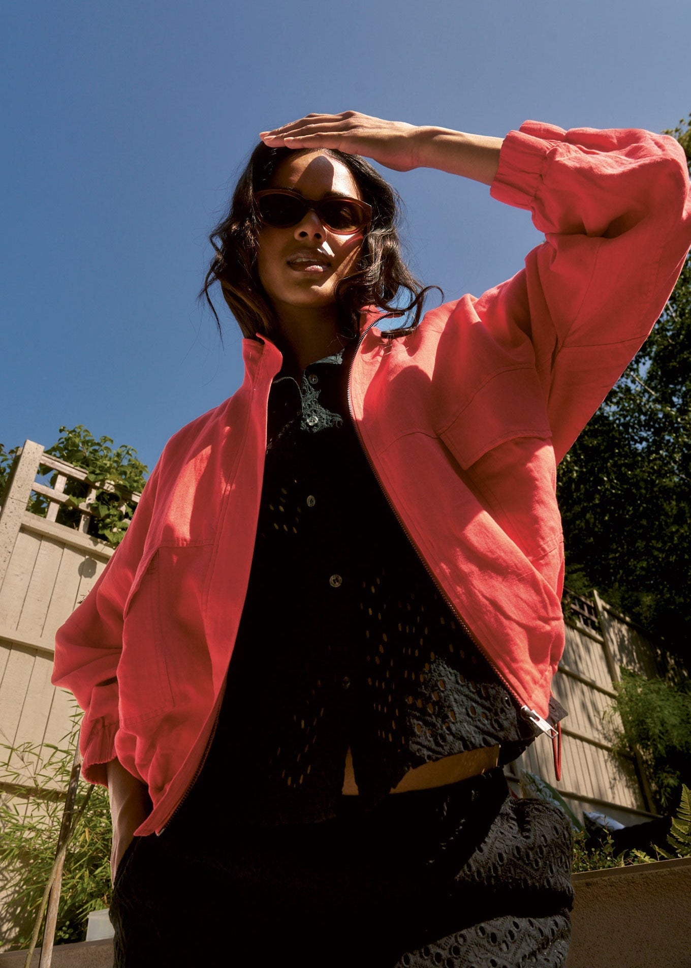 Person wearing a pink jacket and sunglasses outdoors with a clear blue sky.