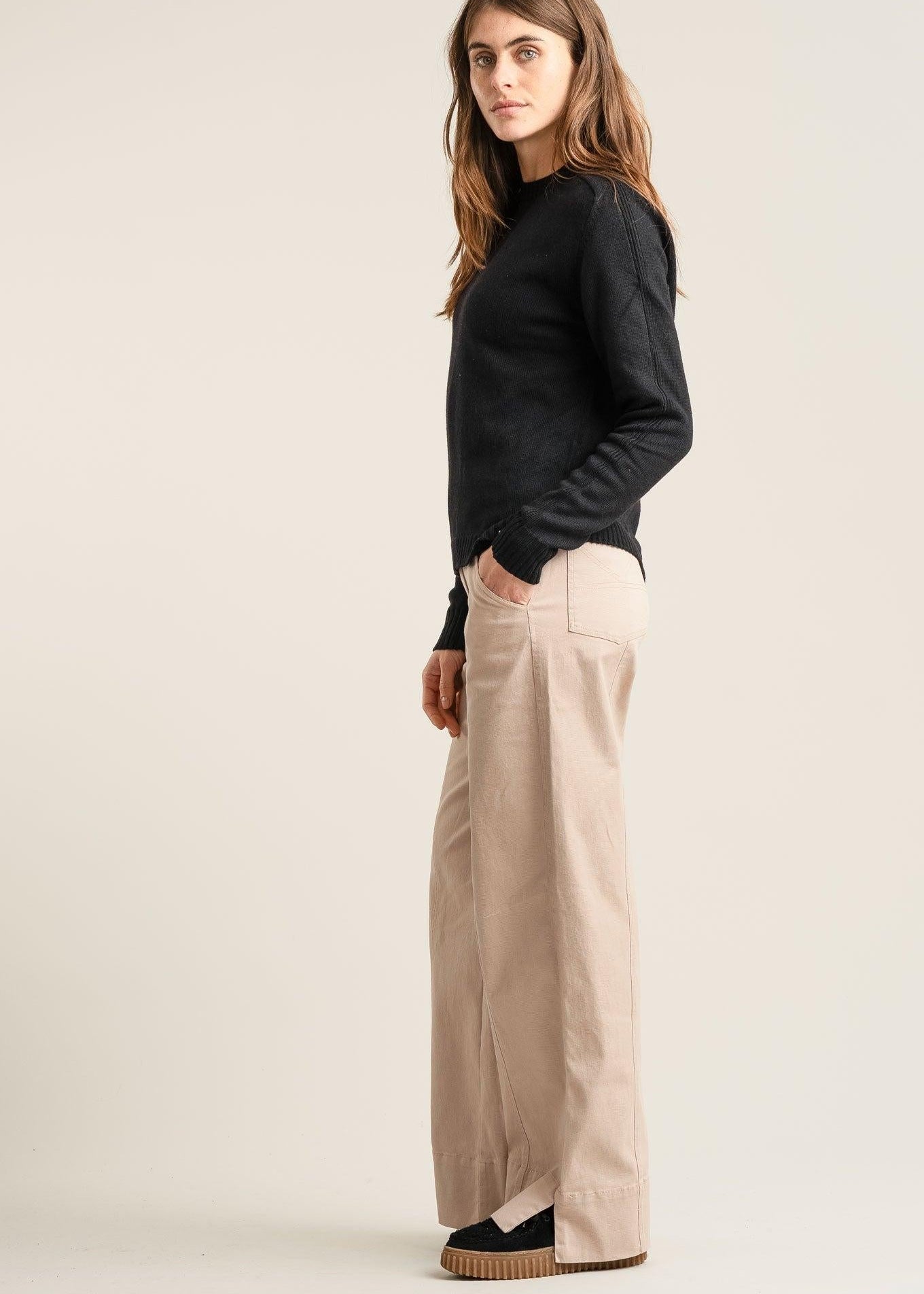 Woman wearing a black top and beige pants on a plain background