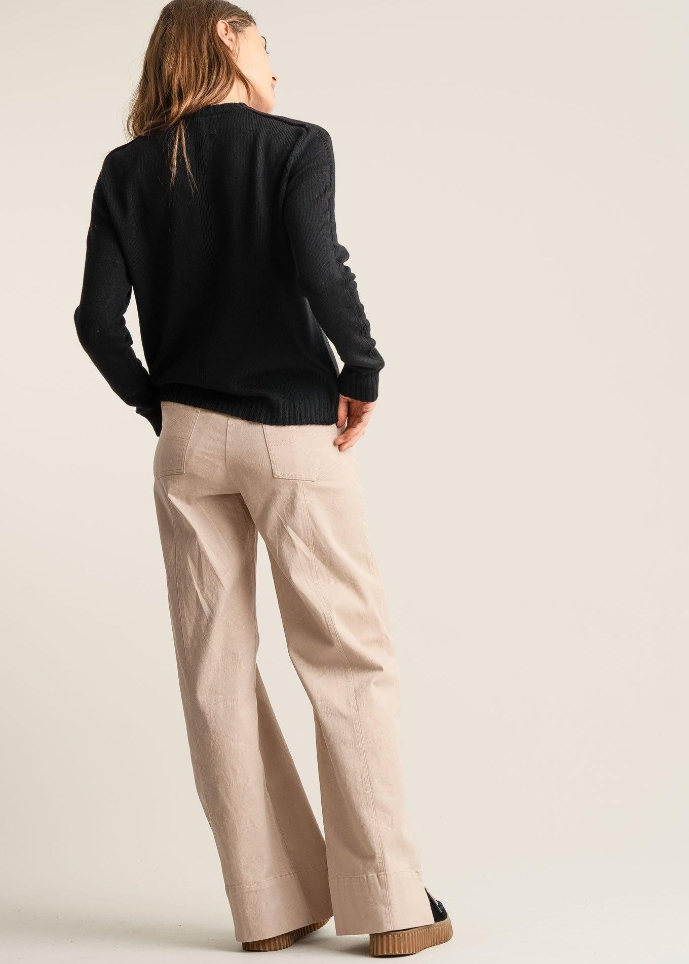 Person wearing a black sweater and beige pants on a plain background
