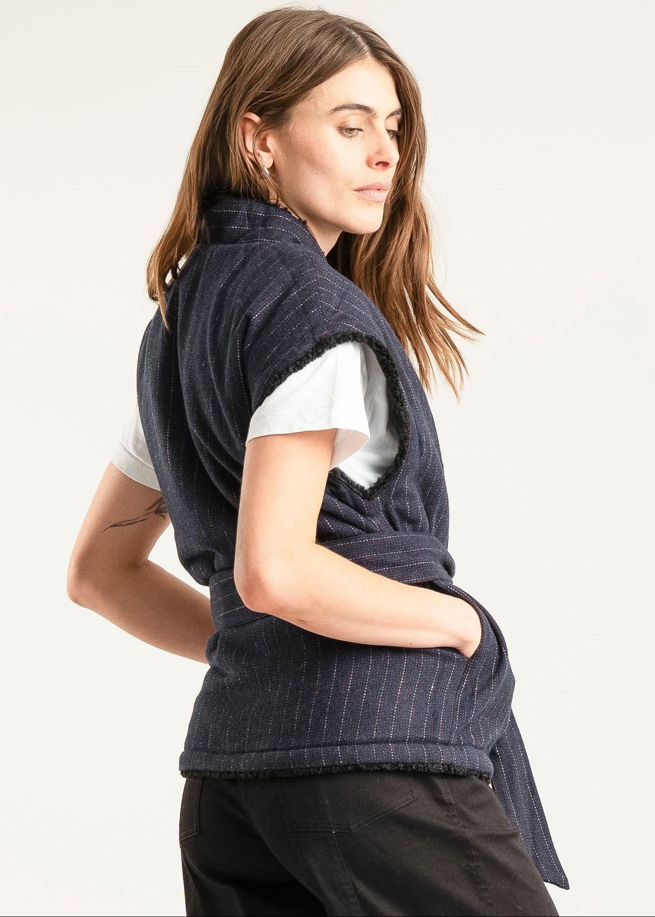 Woman wearing a navy blue knitted shawl over a white shirt on a light gray background