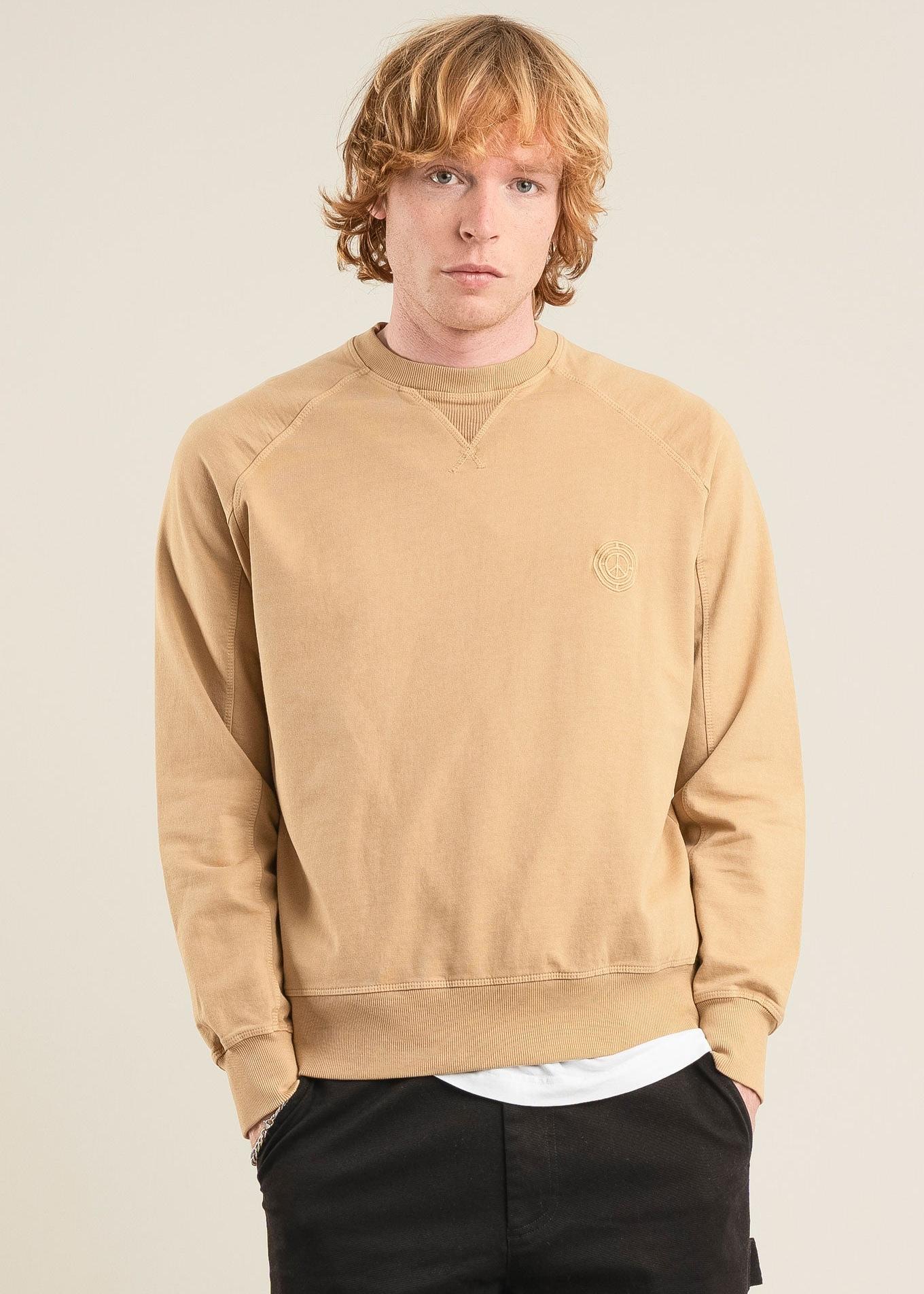 Man wearing a beige sweatshirt with a logo on a plain background