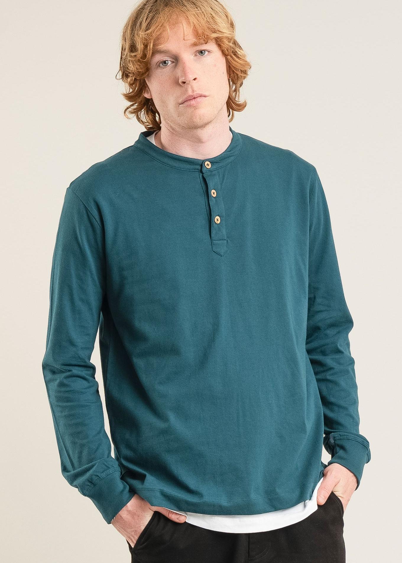 Man wearing a teal long-sleeve shirt against a beige background