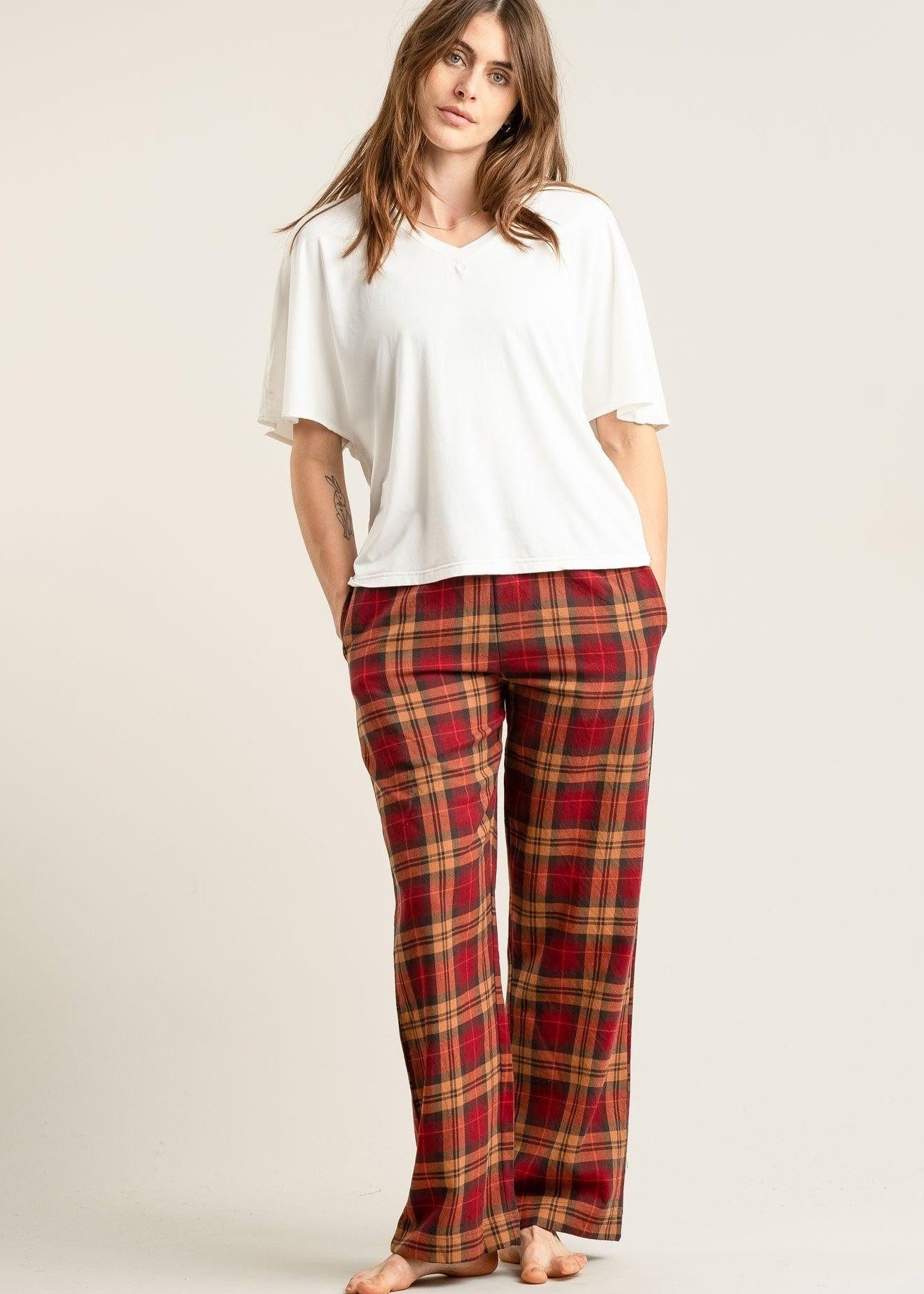 Woman wearing a white top and red plaid pants on a plain background