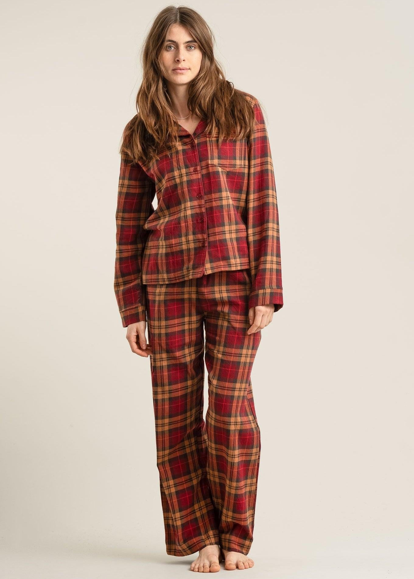 Person wearing a red and brown plaid pajama set on a beige background
