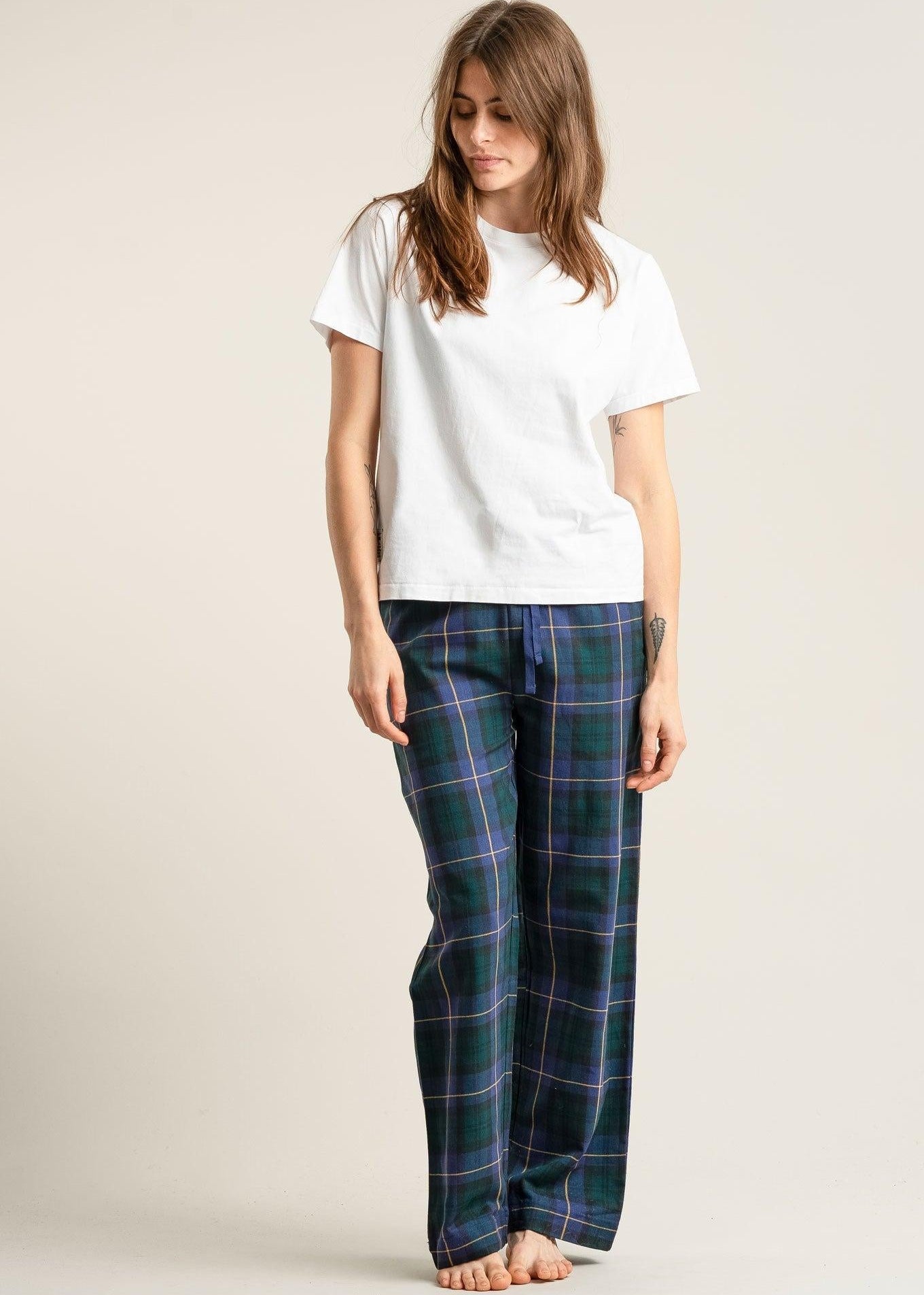 Woman wearing a white t-shirt and blue plaid pajama pants on a plain background