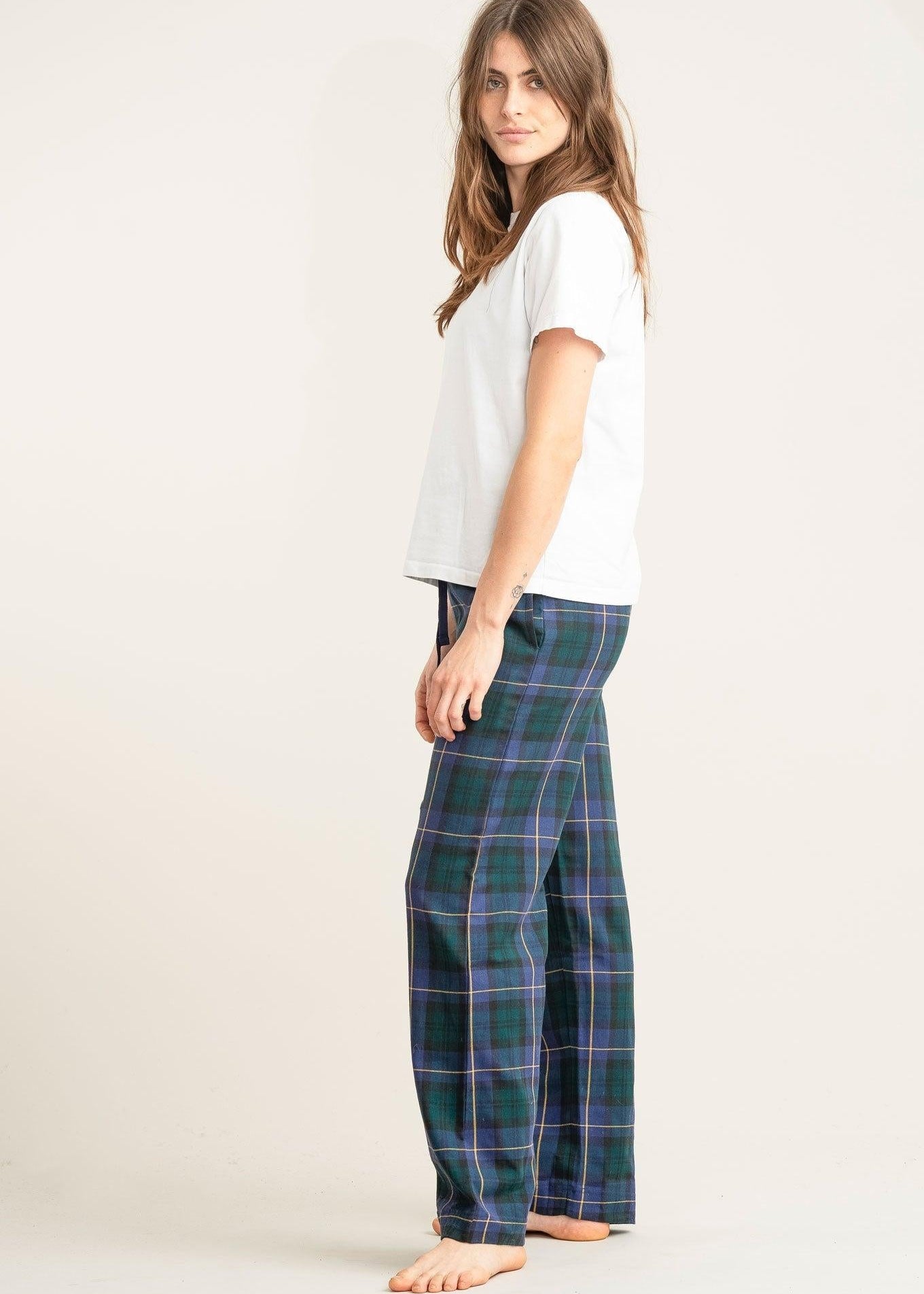 Woman wearing a white t-shirt and green plaid pants on a plain background
