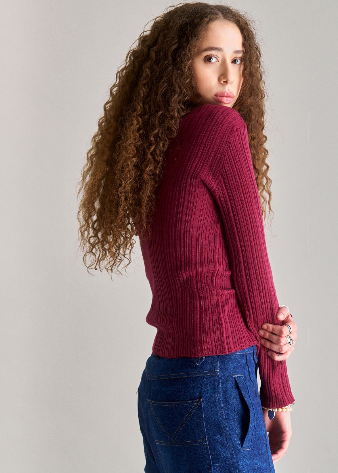 Person wearing a maroon sweater and blue pants against a plain background