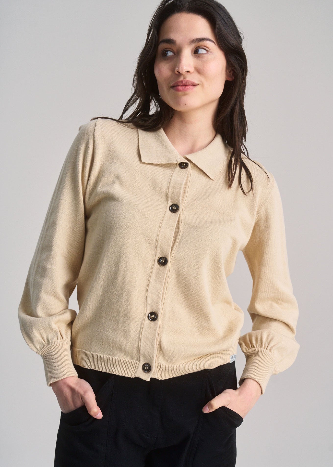 Woman wearing a beige cardigan with black buttons on a plain background