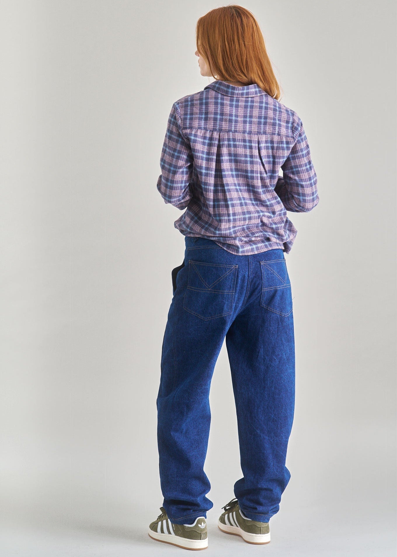 Person wearing a plaid shirt and blue jeans on a plain background