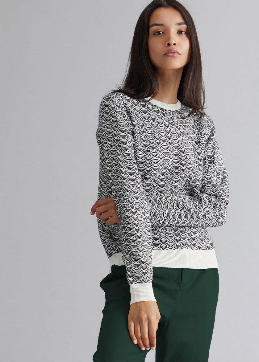 Woman wearing a patterned sweater and green pants on a gray background