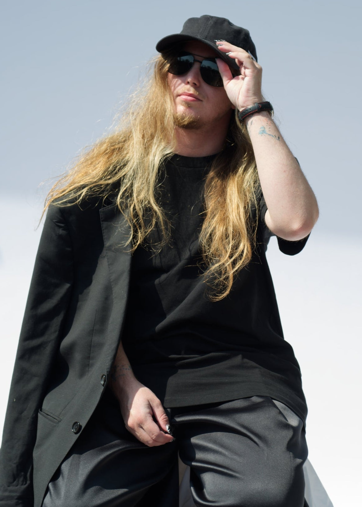 Person wearing a black outfit with sunglasses and a cap against a light blue sky.