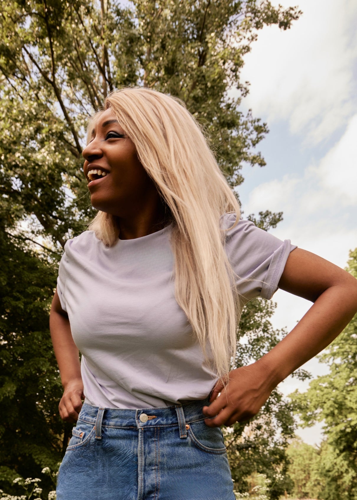 Woman with long blonde hair standing outdoors with trees in the background