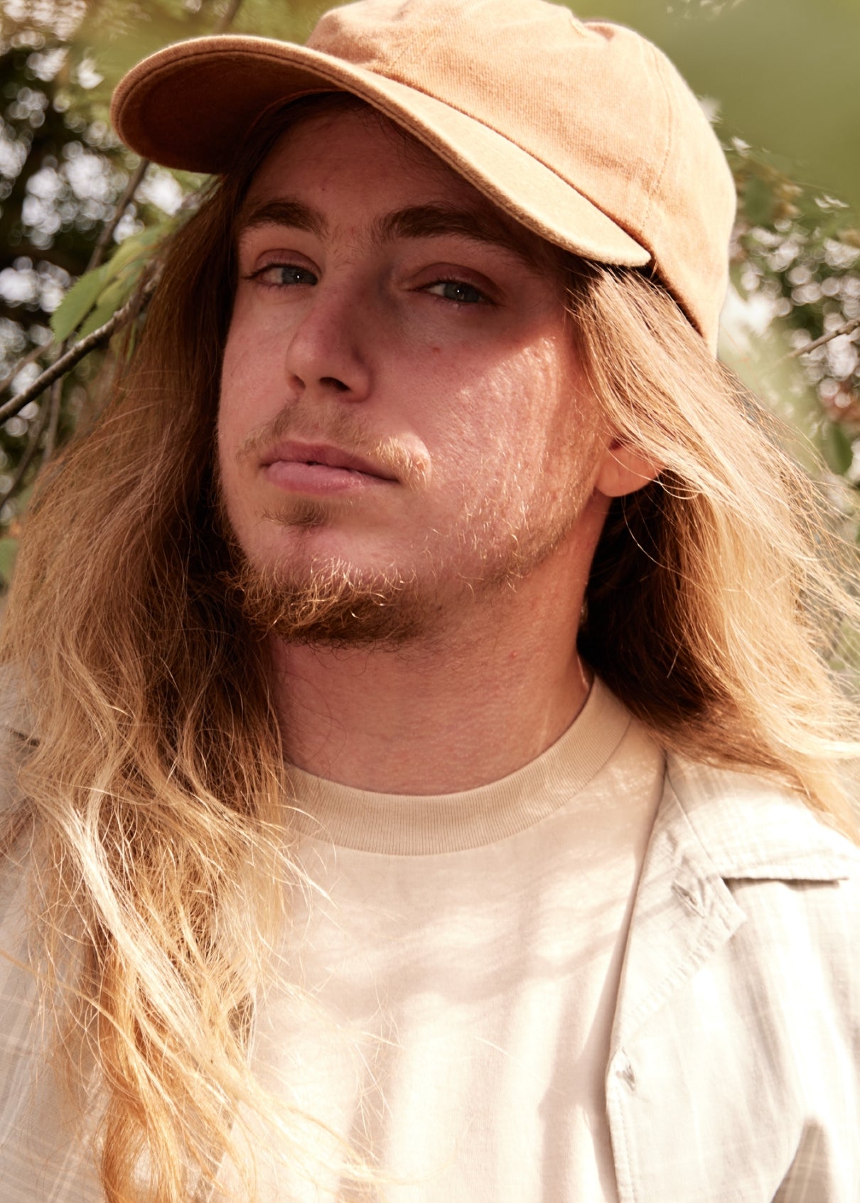 Man with long hair wearing a beige cap and shirt outdoors
