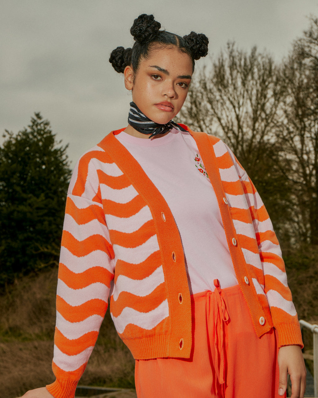 a women wearing an pink shirt with orange trousers and an orange and pink knitted cardigan in a wav 