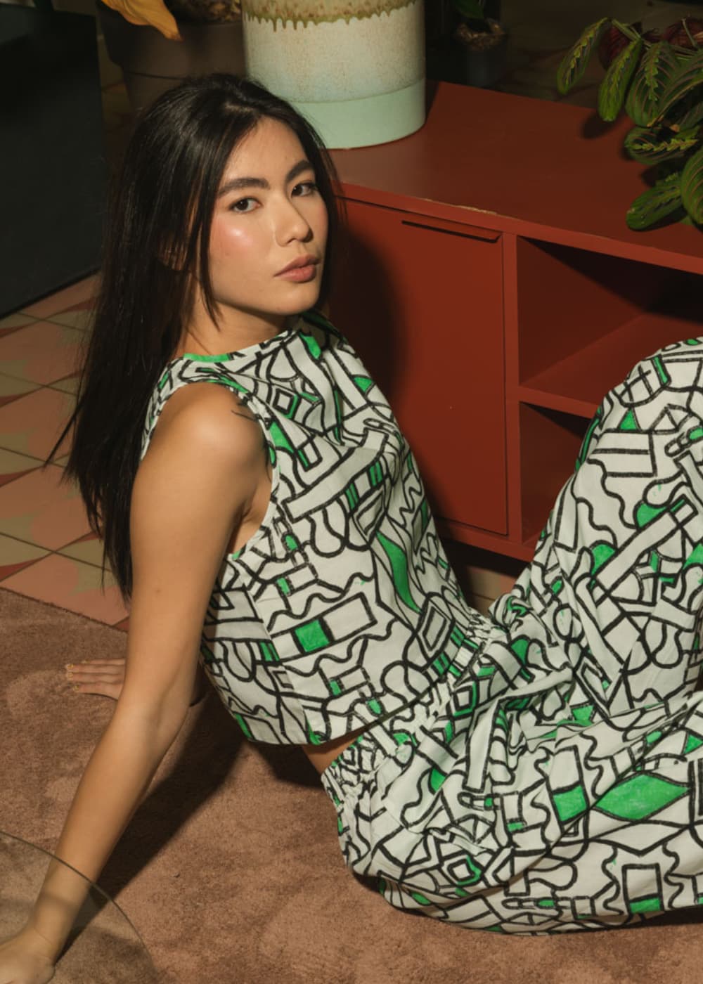 Woman sitting on the floor wearing a patterned dress in an indoor setting.