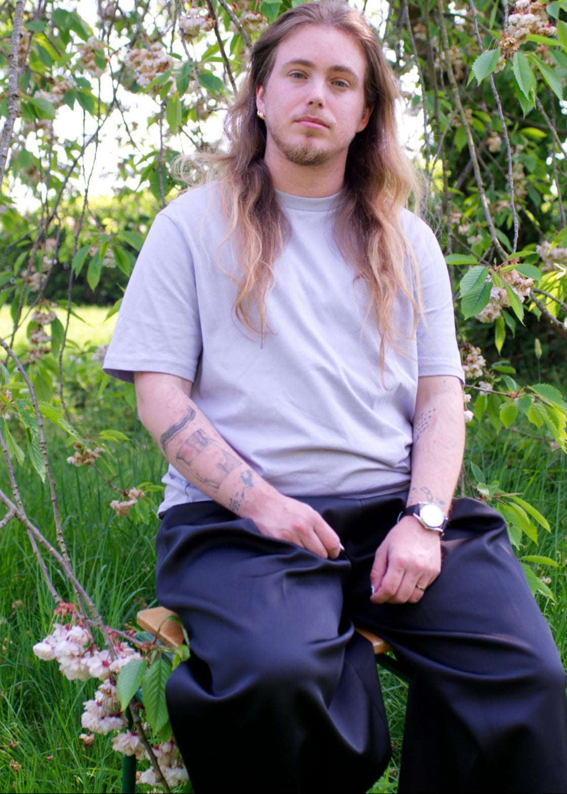 Person with long hair sitting among trees and greenery